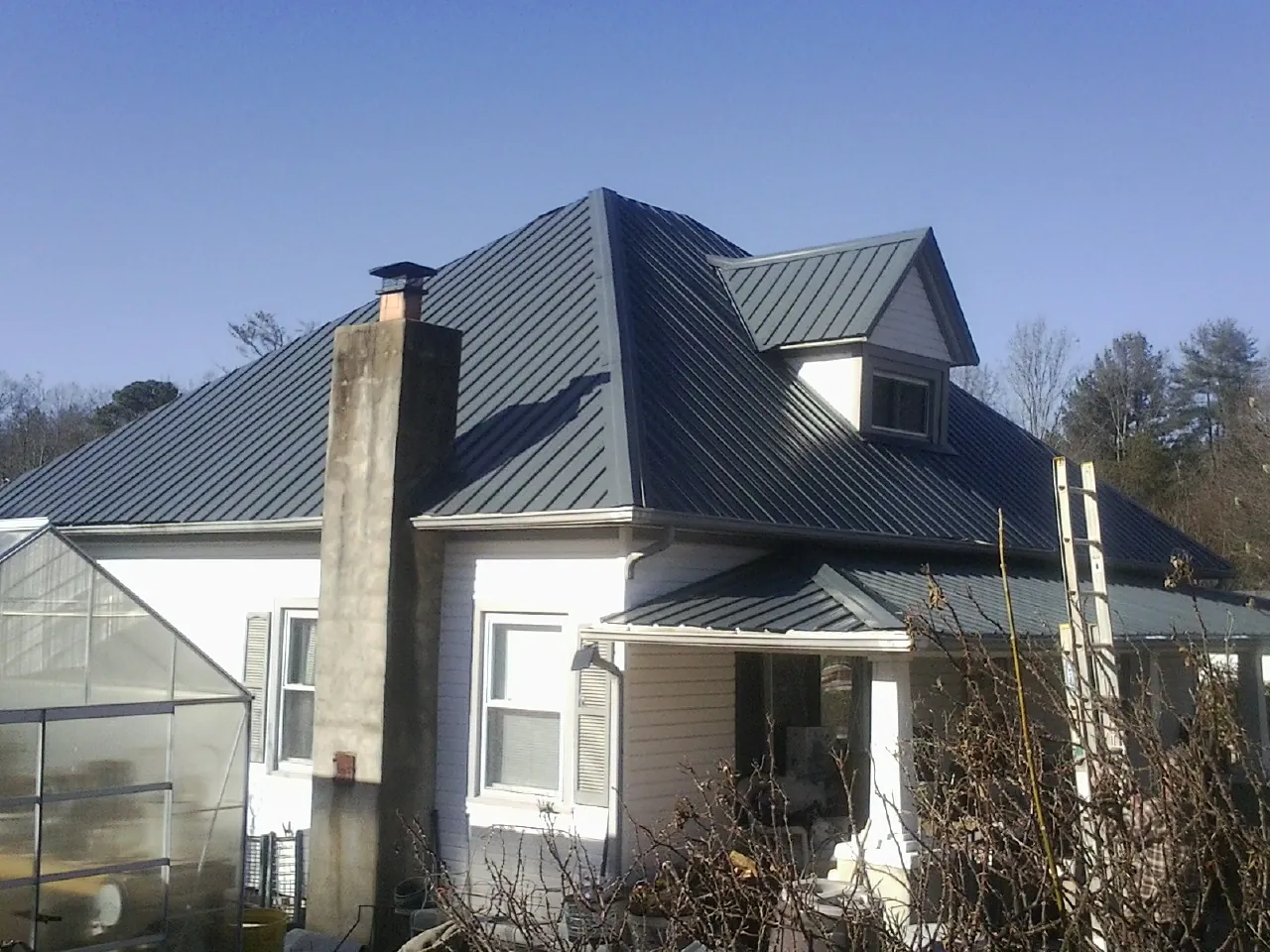 Dark blue standing seam metal roof on a white farmhouse with dormer — Slate & Tile Roof Repair by Roofing Brothers in Jemison