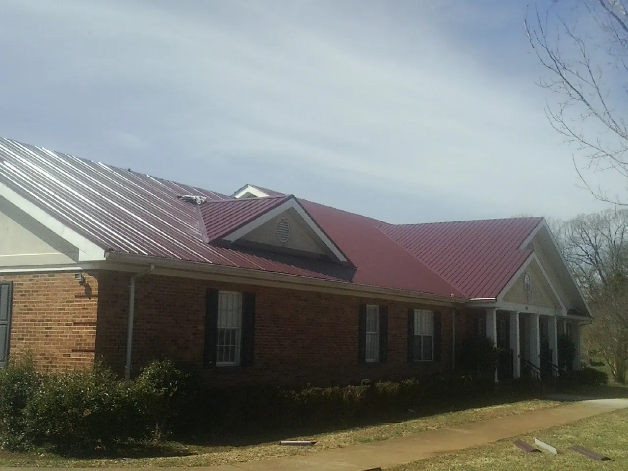 Red metal roof with gabled entries on a long brick building, from a Hail Damage Roof Repair job in Jemison