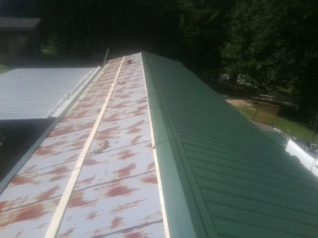 Old rusted panels beside newly installed green metal roofing — Wind Damage Roof Repair by Roofing Brothers in Jemison