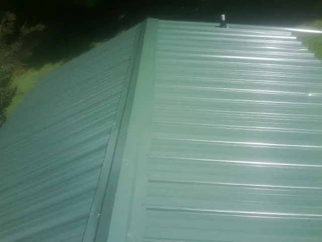 New green metal panels meeting at the ridge of a roof — Flat Roof Repair work by our crew in Jemison