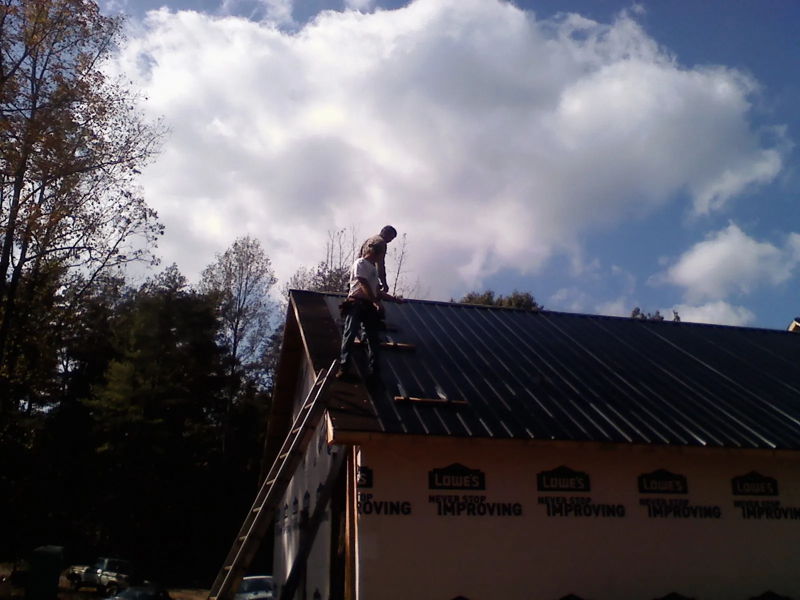 Roofer fastening dark metal panels high against a cloudy sky, from a Roof Inspection job in Jemison