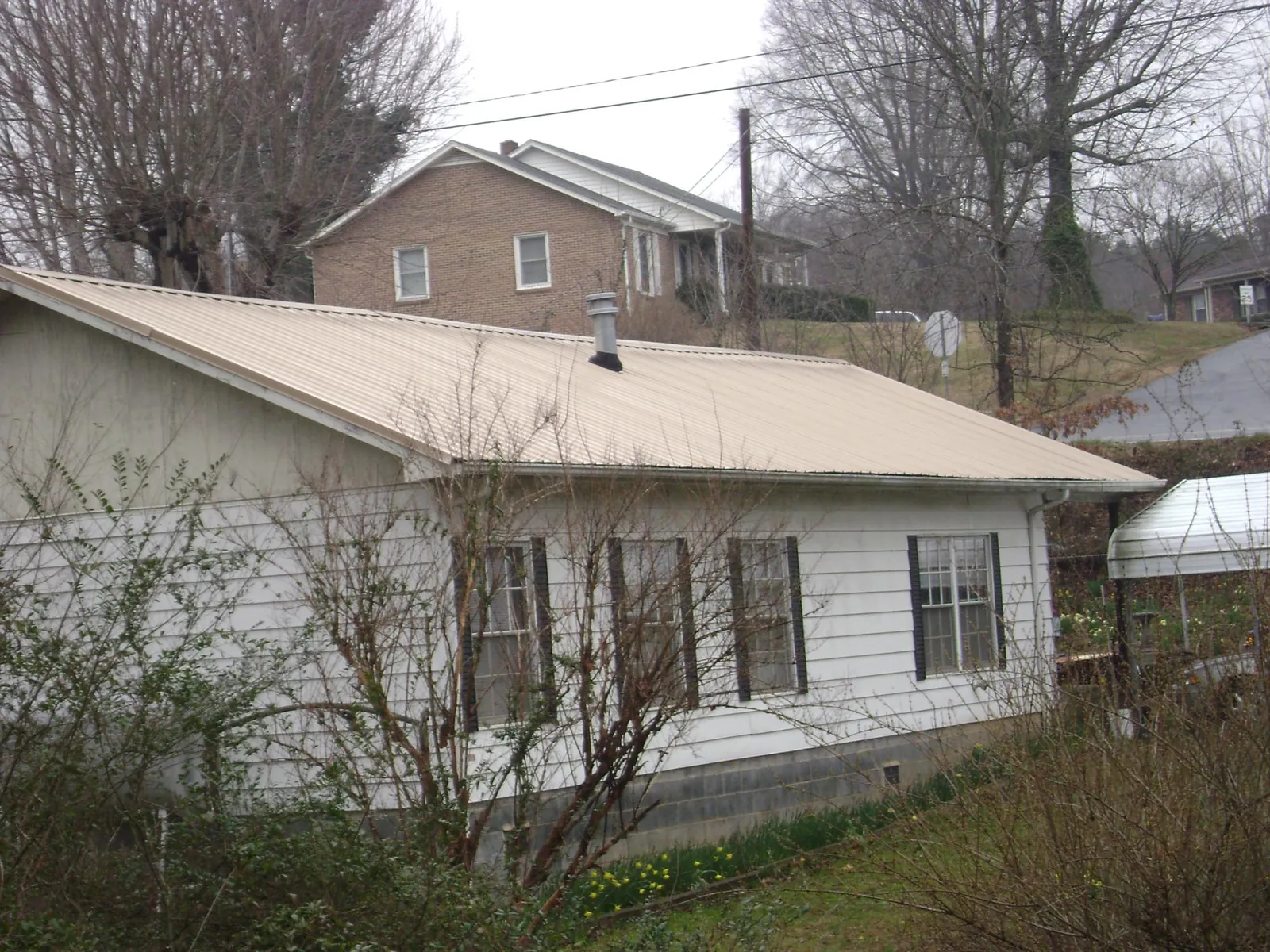 Tan metal roof on a white sided house set into a hillside — Commercial Roofing by Roofing Brothers in Jemison