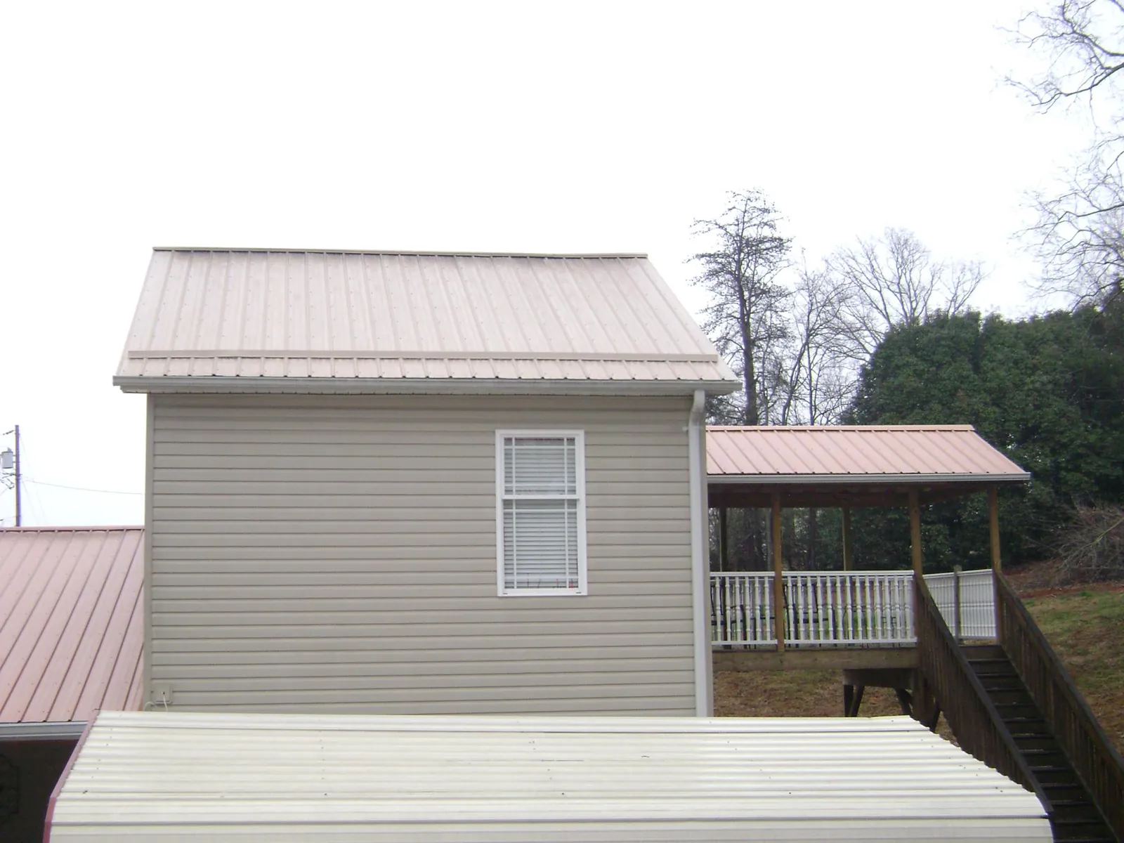Tan metal roofs on a two story addition and attached porch, from a Roof Replacement job in Jemison